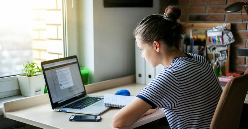 Girl student freelancer working with laptop at home by the window, education and remote work, programmer, online business