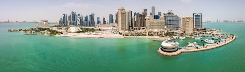 The skyline of Doha, Qatar. Modern rich middle eastern city of skyscrapers, aerial view in good weather, midday, during hot dry summer, with view of marina and beach of Persian Gulf/Arabian Gulf