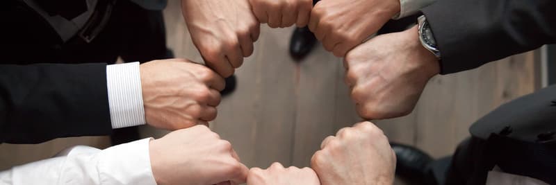 Top above close up view group of businessmen in formal suits standing putting hands fists in circle shape. Teamwork trust motivation support concept, horizontal photo banner for website header design